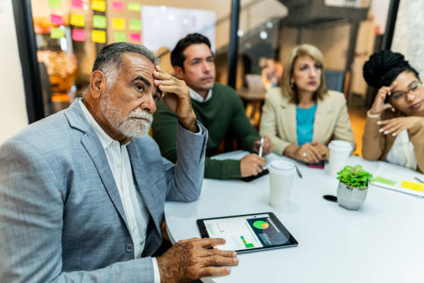 Worried senior businessman listening presentation with coworkers during business meeting at office