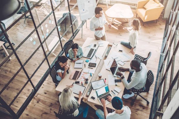 Vista superior de jóvenes creativos multirraciales en una oficina moderna. Grupo de jóvenes empresarios trabajando juntos con ordenadores portátiles, tabletas, teléfonos inteligentes y cuadernos.