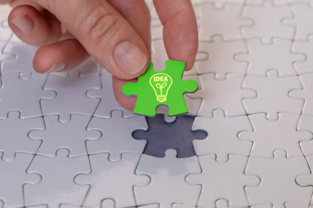 Hand holding last puzzle piece, finishing puzzle with new idea. Close-up of final piece of white blank jigsaw puzzle.