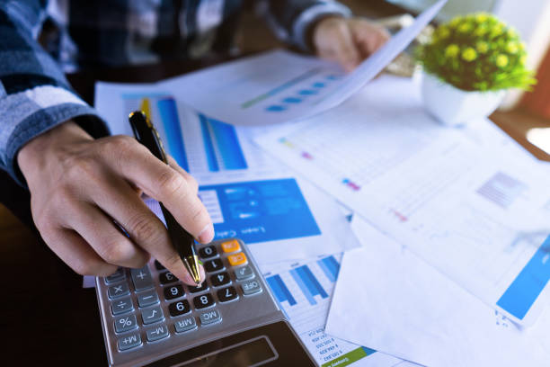 Close up businessman using calculator and reading paper document about business data, accountancy document, graph profit company