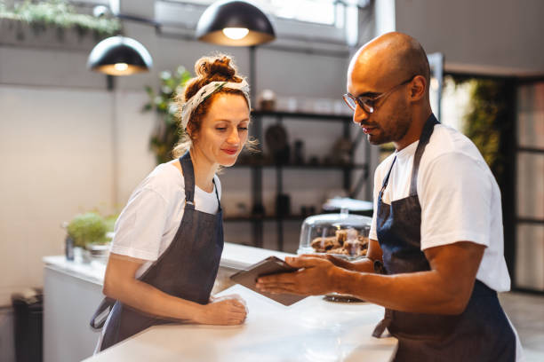 Two service professionals in the hospitality industry use a tablet device to efficiently manage orders and ensure customer satisfaction. Tech savvy waitstaff members working as a team in a cafe.