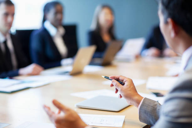 Hands of businessman gesturing ideas decisions with pen pointing leadership to work colleagues in business meeting at board room conference table