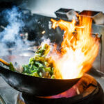 Chef in restaurant kitchen at stove with high burning flames