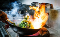 Chef in restaurant kitchen at stove with high burning flames