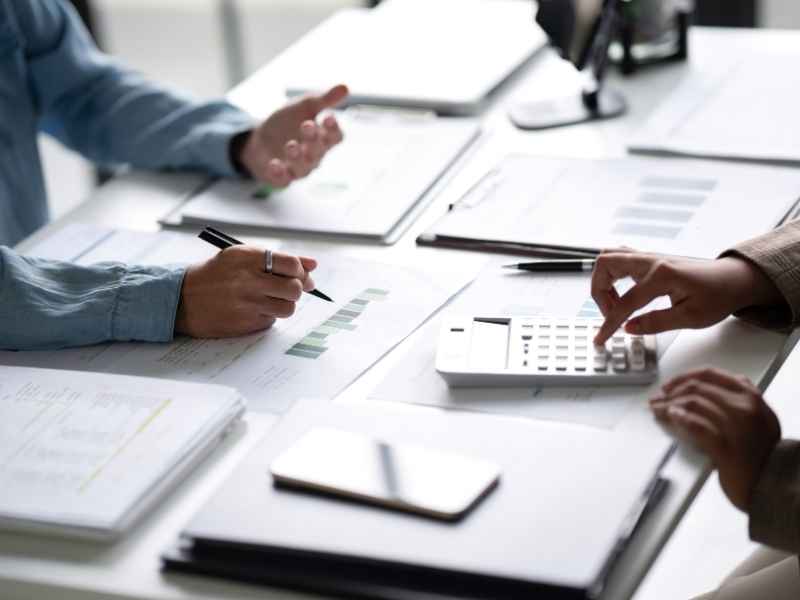 Professionals discussing financial documents and KPI reports at a desk with a calculator and paperwork.