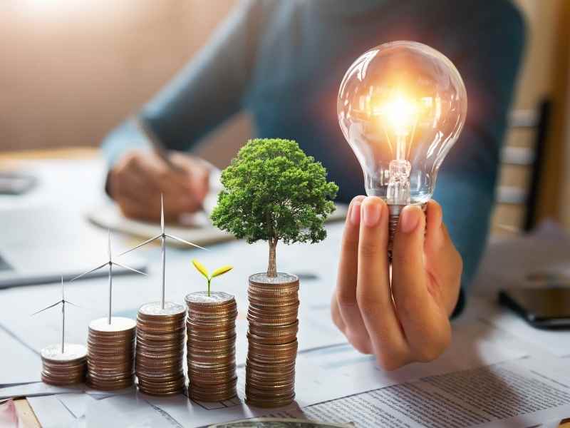 Light bulb and stacked coins with a growing plant, symbolizing energy efficiency, cost savings, and sustainable energy investment.
