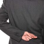 Person in a suit holding hands behind their back, suggesting secrecy and deceptive scam behavior.